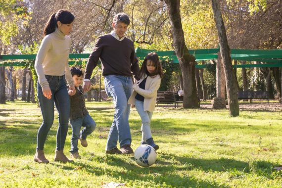 A family plays soccer together in a sunny park, enjoying quality time outdoors.
